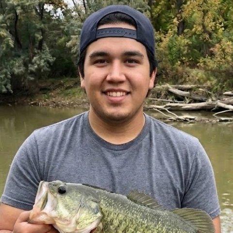 Jorge holding a largemouth bass on a riverbank.
