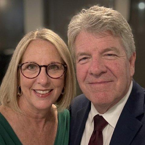 Michelle, a woman with shoulder-length blond hair and glasses, beside a man with grey hair in a suit and tie.